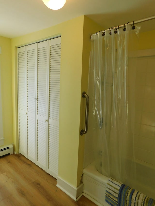 bathroom with a baseboard radiator, wood-type flooring, and shower / tub combo with curtain