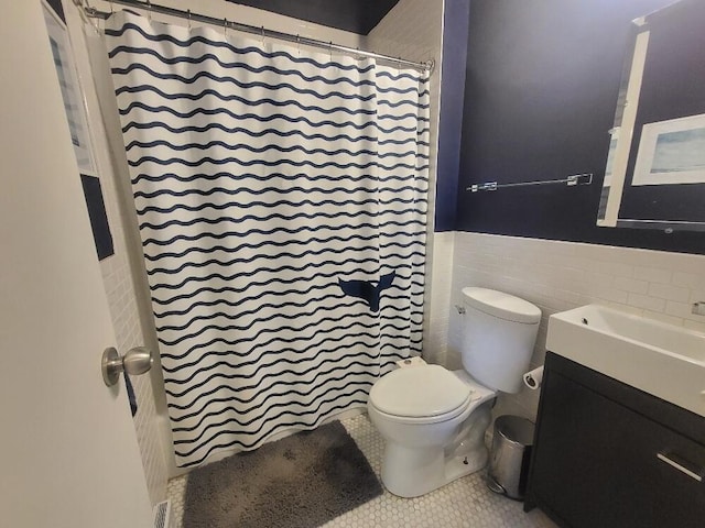 bathroom with toilet, a shower with curtain, tile patterned floors, vanity, and tile walls