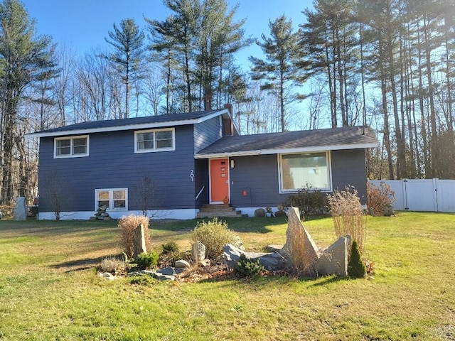 tri-level home featuring entry steps, fence, and a front lawn