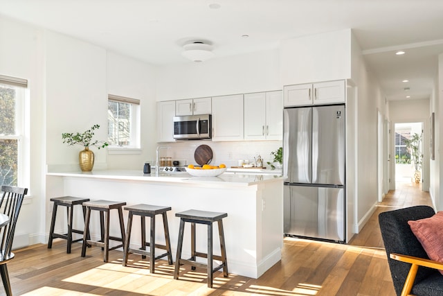 kitchen with kitchen peninsula, appliances with stainless steel finishes, a healthy amount of sunlight, and light hardwood / wood-style flooring