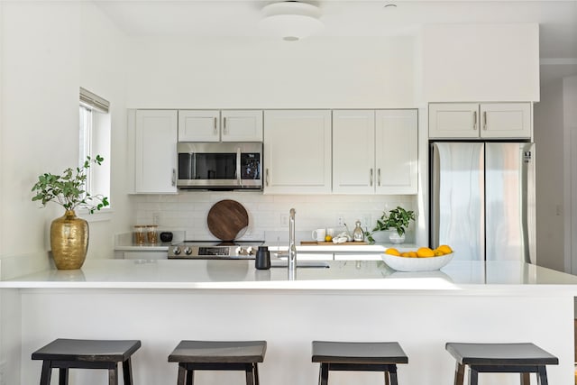 kitchen featuring white cabinetry, kitchen peninsula, stainless steel appliances, and a breakfast bar