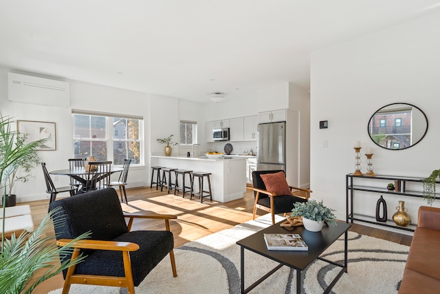 living room with a wall unit AC and light hardwood / wood-style flooring