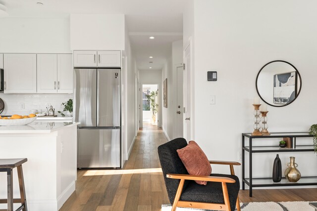 kitchen with stainless steel refrigerator, a kitchen breakfast bar, dark hardwood / wood-style floors, white cabinets, and decorative backsplash