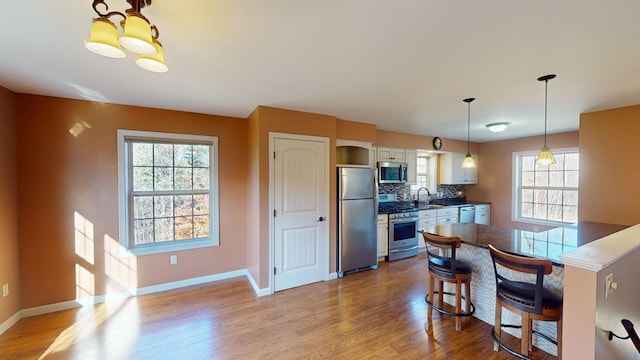 kitchen with stainless steel appliances, light hardwood / wood-style floors, sink, a kitchen bar, and white cabinets