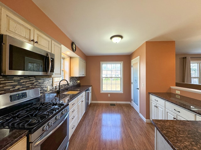 kitchen featuring stainless steel appliances, backsplash, sink, dark wood-type flooring, and dark stone countertops