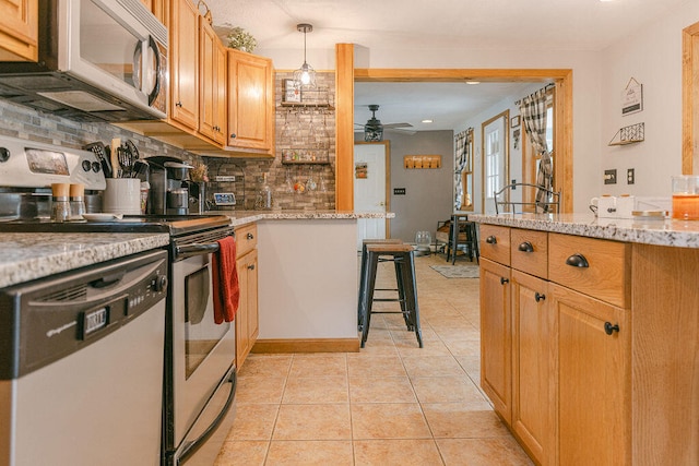 kitchen featuring appliances with stainless steel finishes, decorative light fixtures, light stone countertops, a breakfast bar, and ceiling fan