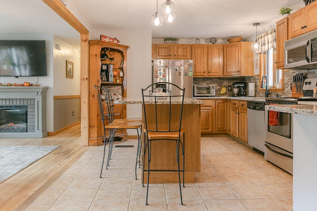 kitchen featuring a kitchen island, appliances with stainless steel finishes, decorative light fixtures, decorative backsplash, and light hardwood / wood-style floors