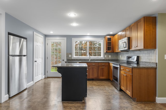 610 W Neck Rd, Nobleboro, ME 04555 - kitchen featuring appliances with stainless steel finishes, decorative backsplash, glass insert cabinets, brown cabinets, and a center island