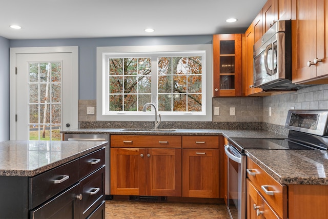 kitchen with appliances with stainless steel finishes, sink, backsplash, and dark stone countertops