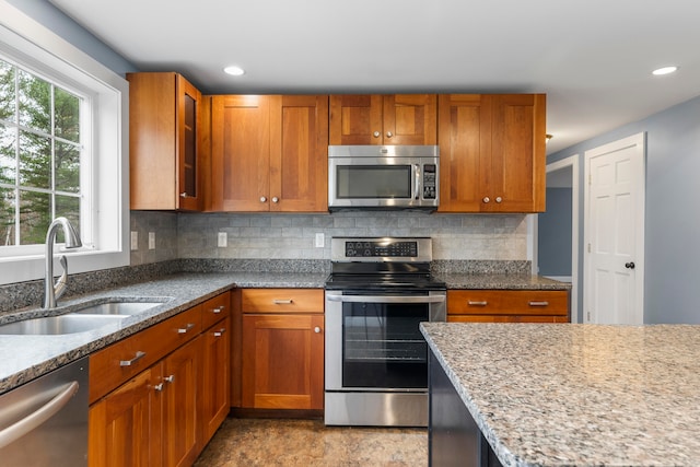 kitchen with tasteful backsplash, appliances with stainless steel finishes, sink, and light stone counters