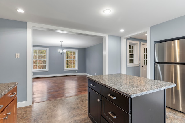 kitchen featuring light stone counters, hanging light fixtures, a center island, stainless steel fridge, and light wood-type flooring