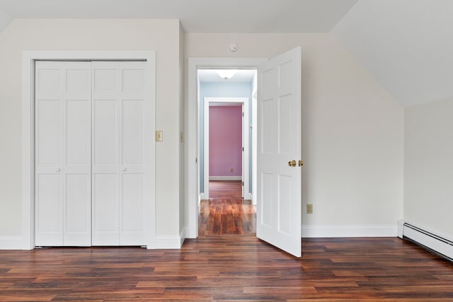 unfurnished bedroom with dark hardwood / wood-style floors, a closet, a baseboard heating unit, and vaulted ceiling