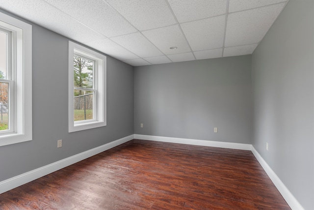 empty room with a paneled ceiling, dark wood-type flooring, and a healthy amount of sunlight