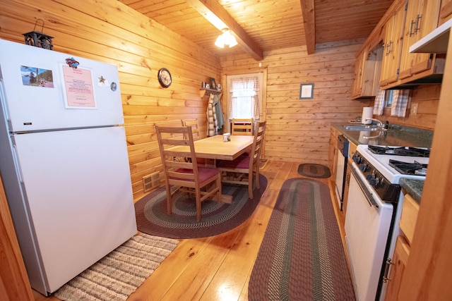 kitchen with beamed ceiling, wooden walls, white appliances, sink, and light hardwood / wood-style floors