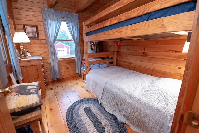 bedroom featuring beamed ceiling, light hardwood / wood-style flooring, and wooden walls