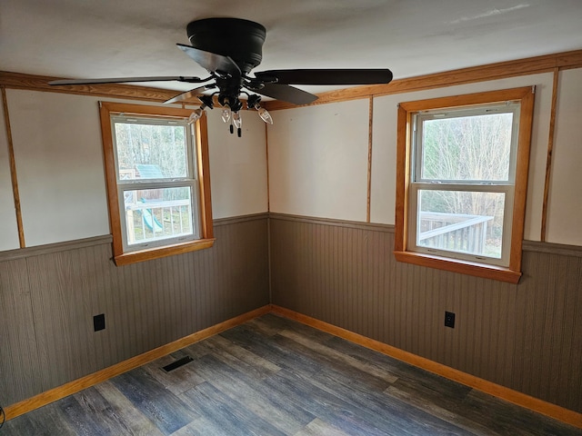 spare room featuring ceiling fan, wooden walls, dark wood-type flooring, and a wealth of natural light