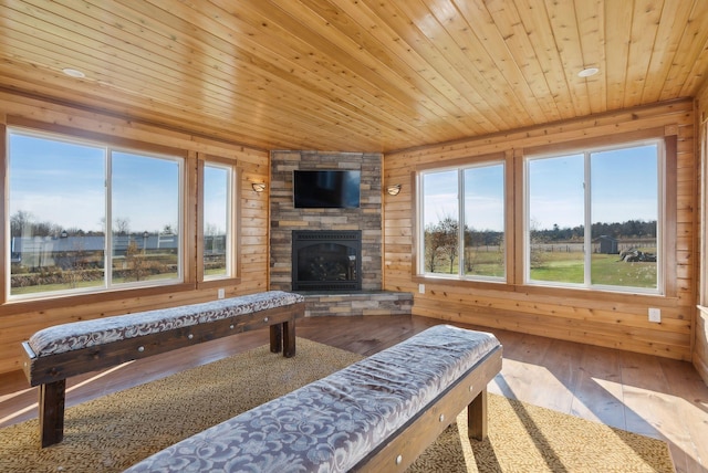 living room with wood ceiling, hardwood / wood-style flooring, a stone fireplace, and wood walls