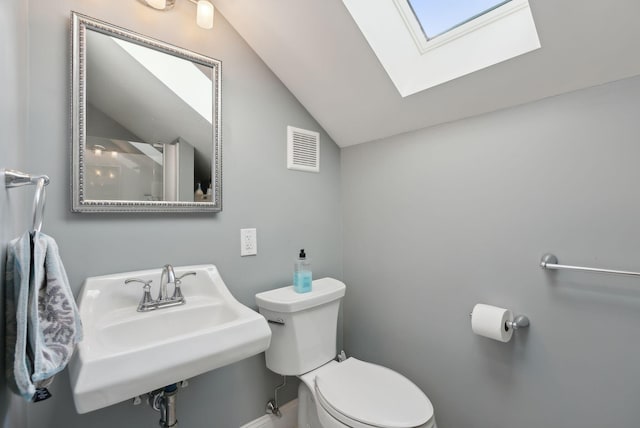 bathroom featuring sink, vaulted ceiling with skylight, and toilet