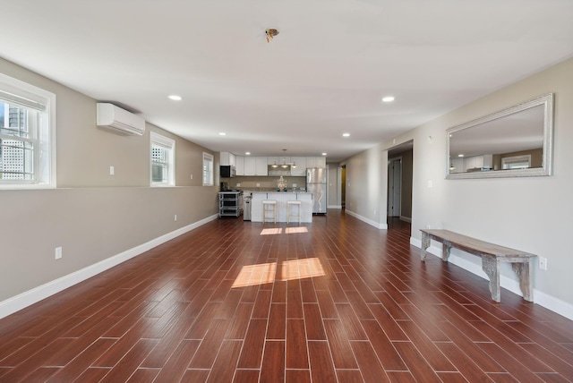 unfurnished living room with a wall mounted AC, dark hardwood / wood-style floors, and plenty of natural light