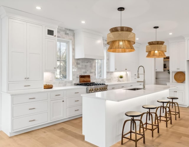 kitchen with sink, custom exhaust hood, hanging light fixtures, a center island with sink, and stove