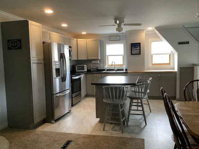 kitchen with gray cabinets, a center island, appliances with stainless steel finishes, and ceiling fan