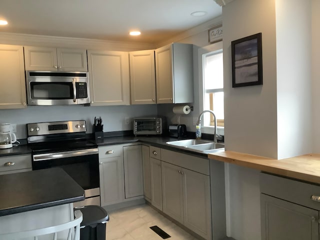 kitchen with wooden counters, sink, stainless steel appliances, and gray cabinets