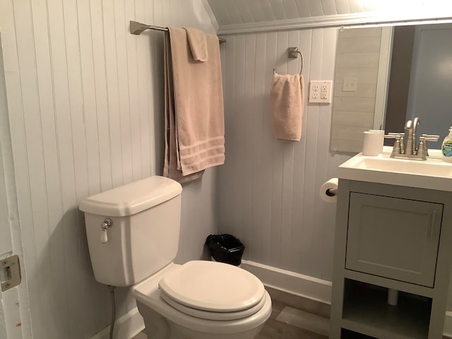 bathroom with vanity, toilet, and wood walls