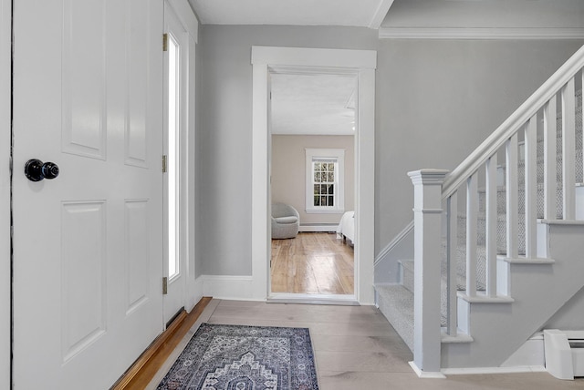 foyer entrance with baseboard heating, light wood-type flooring, and crown molding