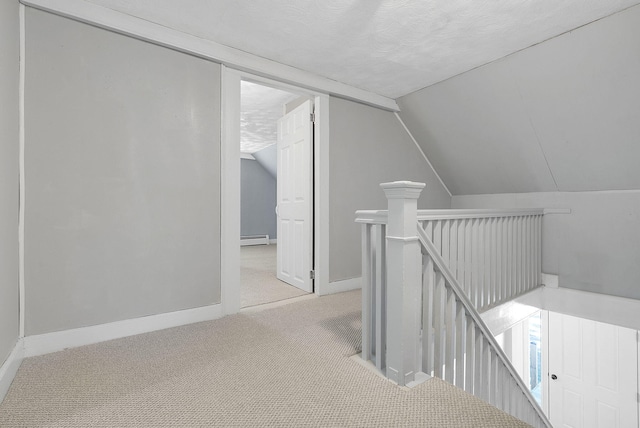 hall with a textured ceiling, vaulted ceiling, light colored carpet, and a baseboard heating unit