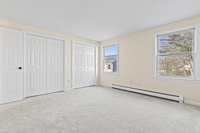 unfurnished bedroom with light colored carpet, multiple closets, multiple windows, and a baseboard heating unit