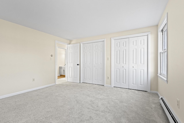 unfurnished bedroom featuring multiple closets, light colored carpet, and a baseboard heating unit