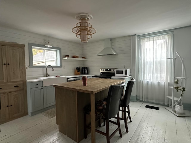 kitchen with ventilation hood, stainless steel appliances, butcher block counters, a kitchen island, and a kitchen breakfast bar