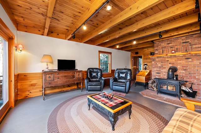 living room featuring beam ceiling, rail lighting, a wood stove, and wooden walls