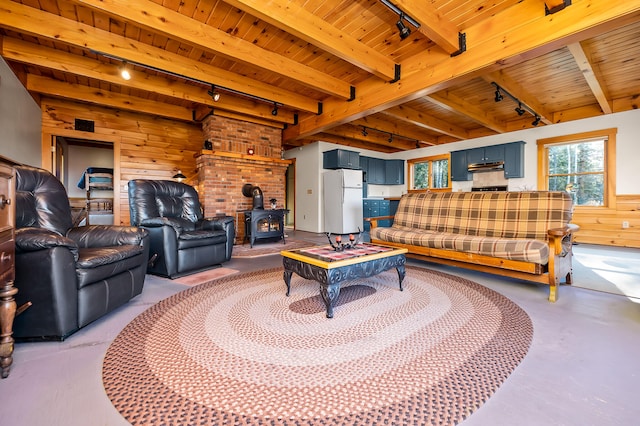 living room featuring beam ceiling, a wood stove, rail lighting, wooden ceiling, and wood walls