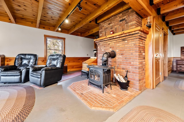 living room featuring beam ceiling, a wood stove, wood walls, and rail lighting