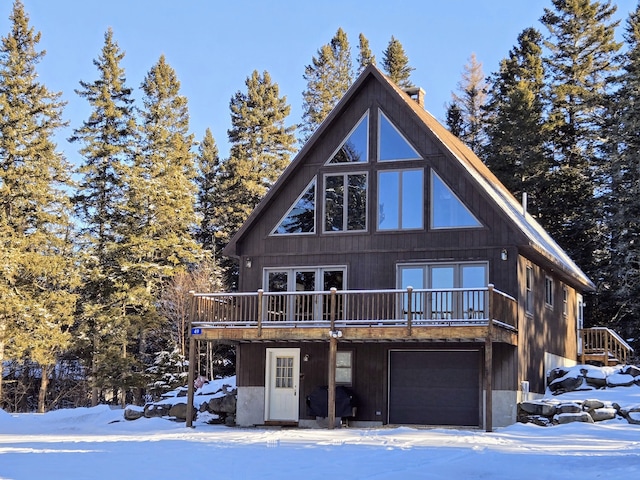 snow covered rear of property featuring a garage and a deck