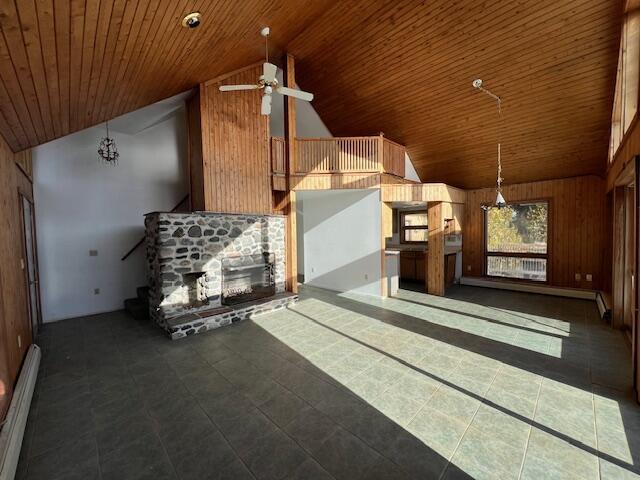 interior space featuring a stone fireplace, wooden walls, high vaulted ceiling, a baseboard heating unit, and ceiling fan with notable chandelier