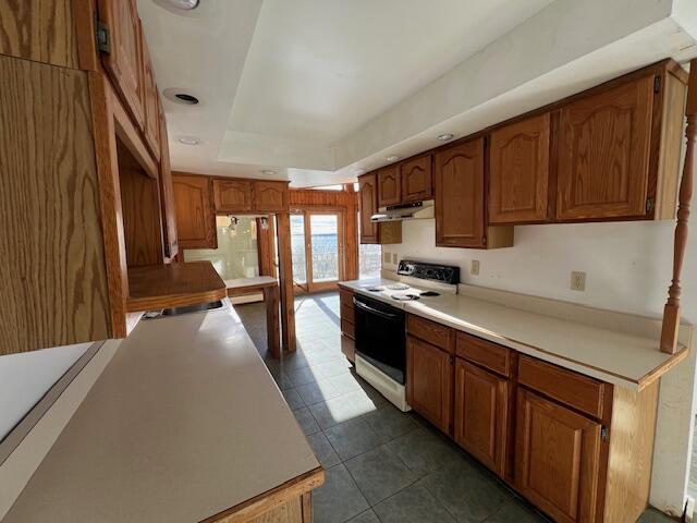 kitchen with a raised ceiling, white range with electric stovetop, and dark tile patterned flooring