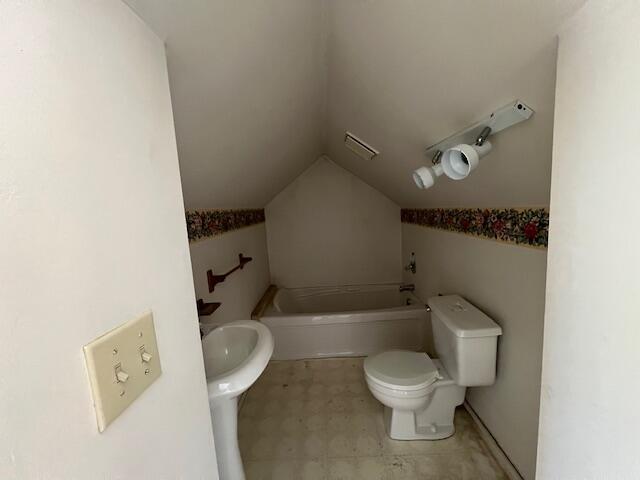 bathroom featuring a bathtub, lofted ceiling, and toilet