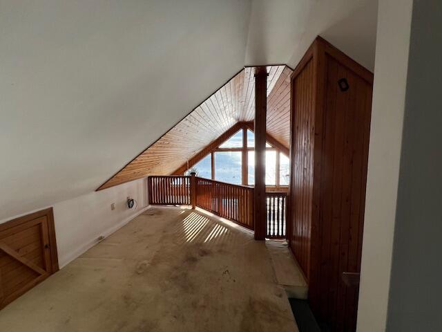 additional living space with wooden walls, carpet floors, and vaulted ceiling