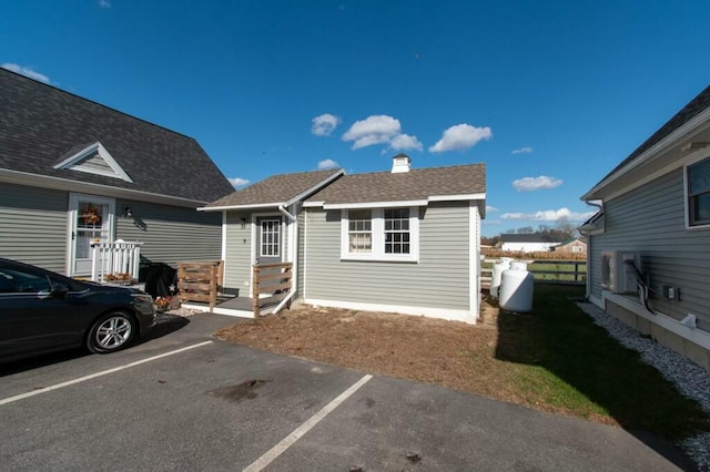 rear view of property featuring roof with shingles, uncovered parking, and a chimney