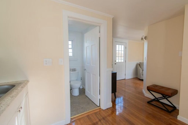 corridor featuring wood finished floors, baseboards, and a sink