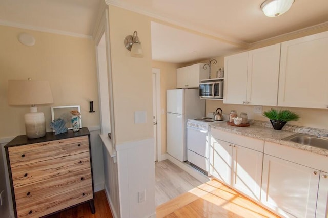 kitchen with white appliances, white cabinets, light wood-style floors, a sink, and ornamental molding