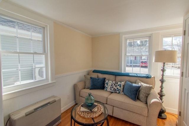 living area with wood finished floors, a wainscoted wall, and crown molding