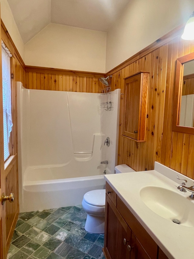 full bathroom with lofted ceiling, toilet, wooden walls, vanity, and bathtub / shower combination