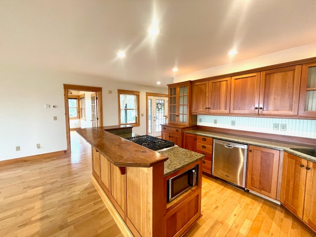 kitchen with stainless steel appliances, light hardwood / wood-style flooring, dark stone countertops, a breakfast bar, and a kitchen island