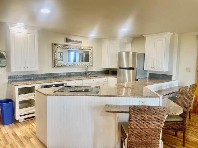 kitchen featuring kitchen peninsula, appliances with stainless steel finishes, sink, light hardwood / wood-style flooring, and white cabinets