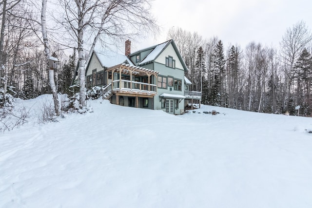 snow covered back of property featuring a pergola and a wooden deck