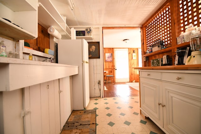 kitchen with white cabinets, wooden walls, and white fridge