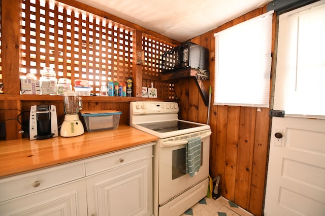 kitchen with wooden counters, white electric range, wood walls, and white cabinets